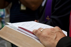 A priest holds a bible and prayin' with other people.